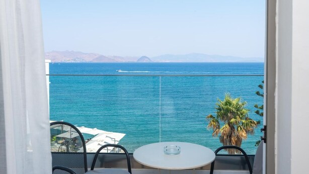 Un balcón con mesa y sillas, con vista al mar tranquilo y montañas a lo lejos.
