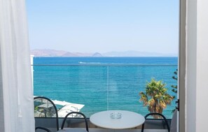 Un balcón con mesa y sillas, con vista al mar tranquilo y montañas a lo lejos.