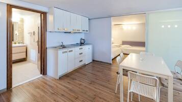 Una cocina compacta con armarios blancos, un lavamanos y una estufa. Hay un comedor con una mesa y sillas.