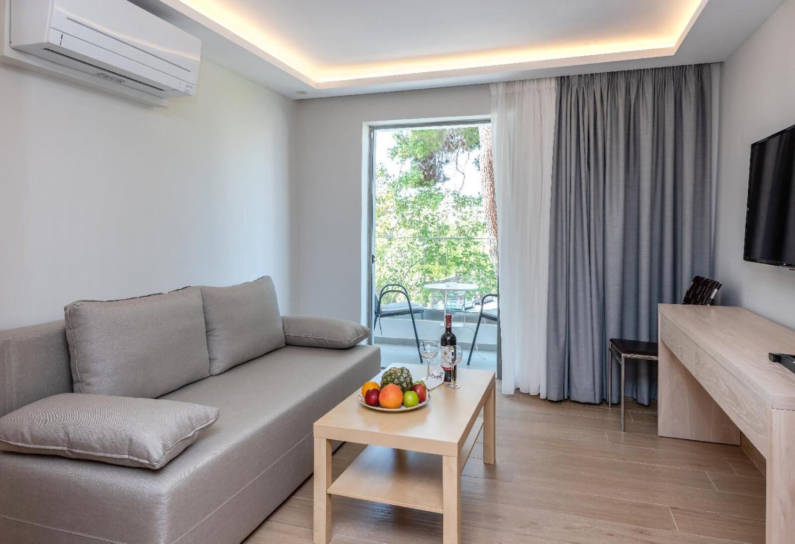 Een moderne woonkamer met een bank, een klein tafeltje met fruit, een televisie en een balkon met uitzicht.