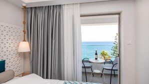 Habitación de hotel con cama, mesita de noche, lámpara, ventana con cortinas y balcón con mesa y sillas.
