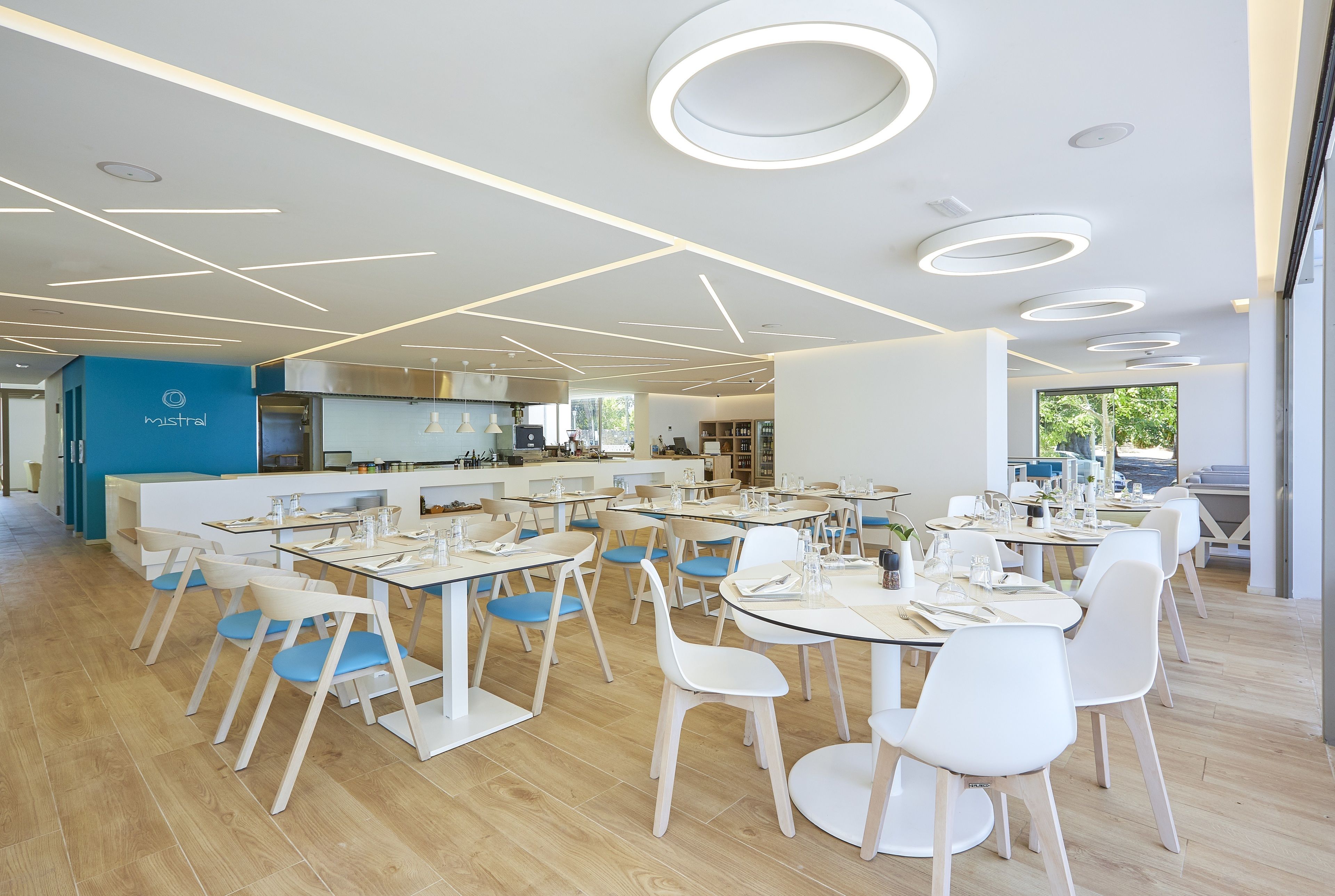 Un espace de restauration moderne avec des tables et des chaises rondes, une cuisine en arrière-plan et un mur d’accent bleu.