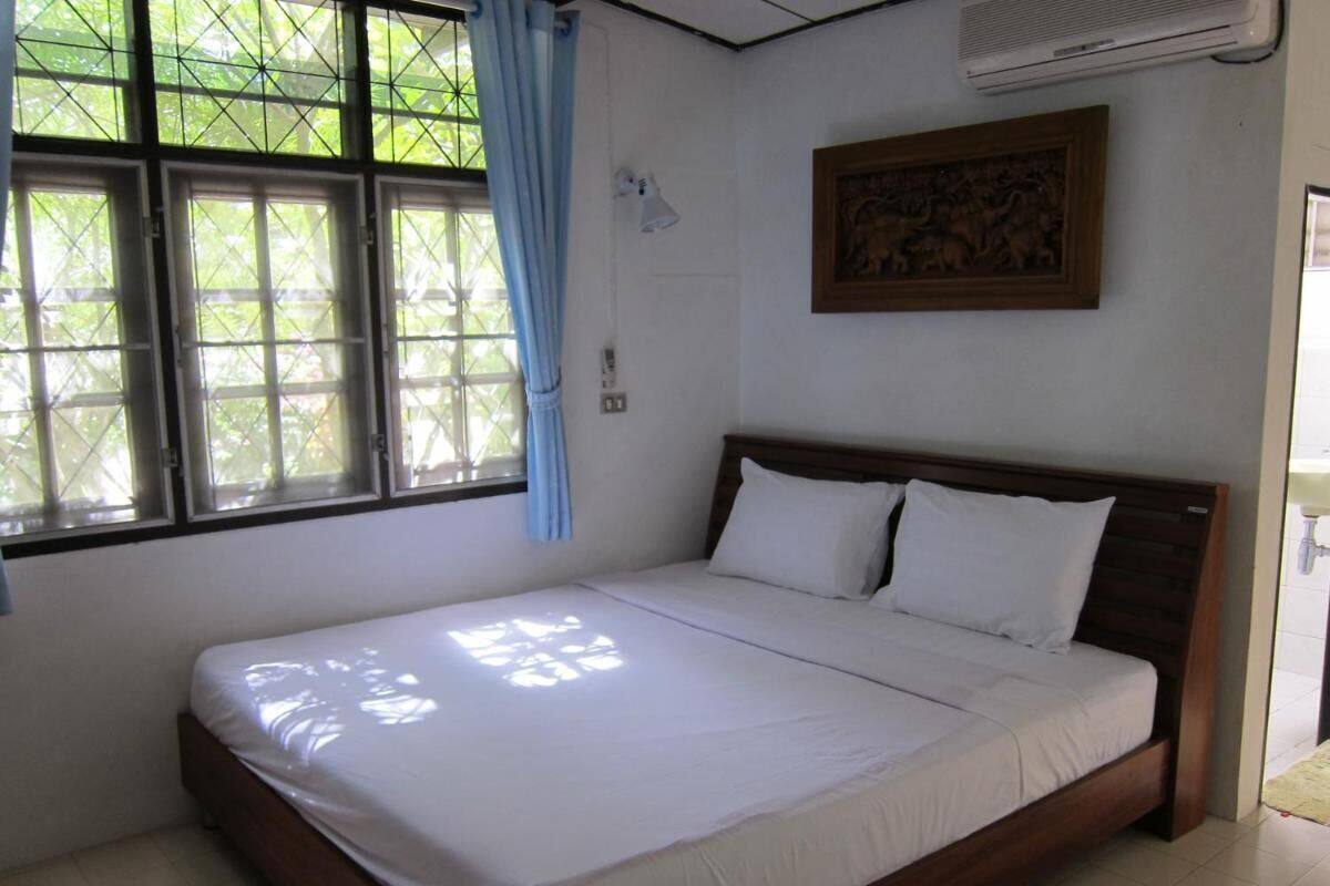 A bedroom with a single bed, a window with curtains, a wall-mounted air conditioner, and a framed picture on the wall.