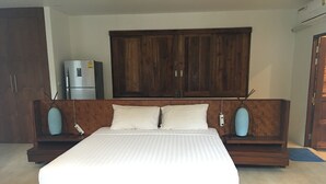 A large bed with a wooden frame and white bedding, flanked by wooden nightstands with blue lamps, in a room with wooden cabinets and a built-in wardrobe. - Bang Po Village (Koh Samui)