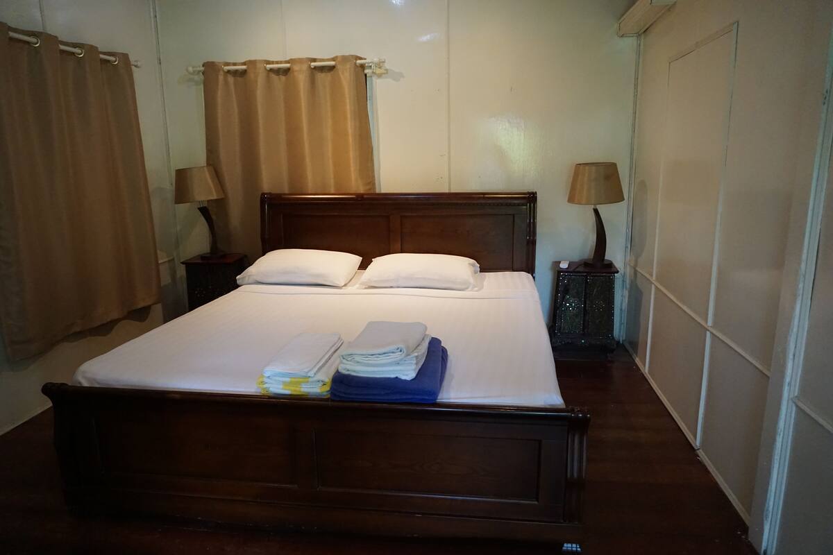 A neatly made bed with pillows and folded towels, two bedside lamps, and a wooden headboard.