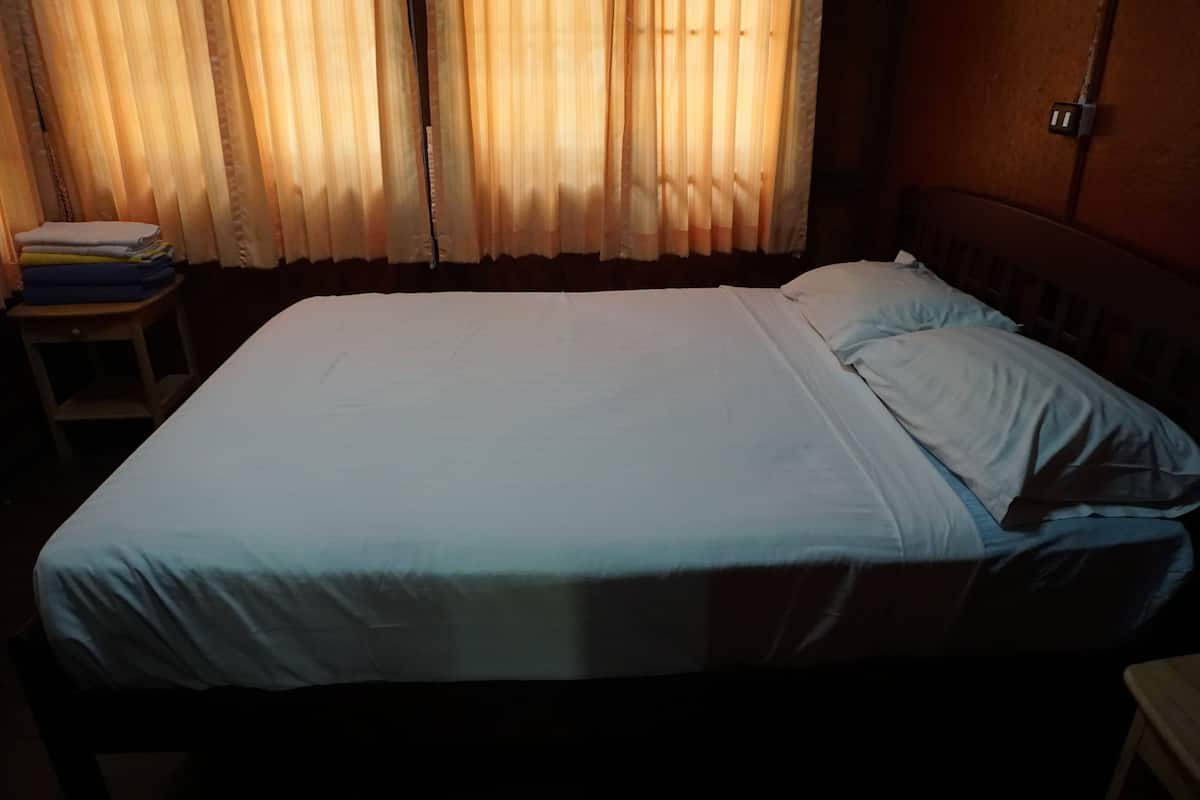 A bed with a white sheet and a pillow, a wooden headboard, and a small table with folded items.