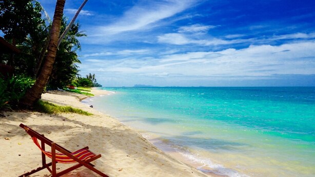 A beach with a hammock and a wooden chair on the sand, palm trees, and a clear blue sky. - Bang Po Village (Koh Samui)
