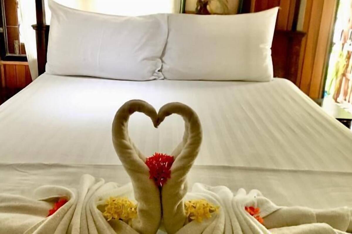 A hotel room with a bed, pillows, and a heart-shaped towel arrangement.
