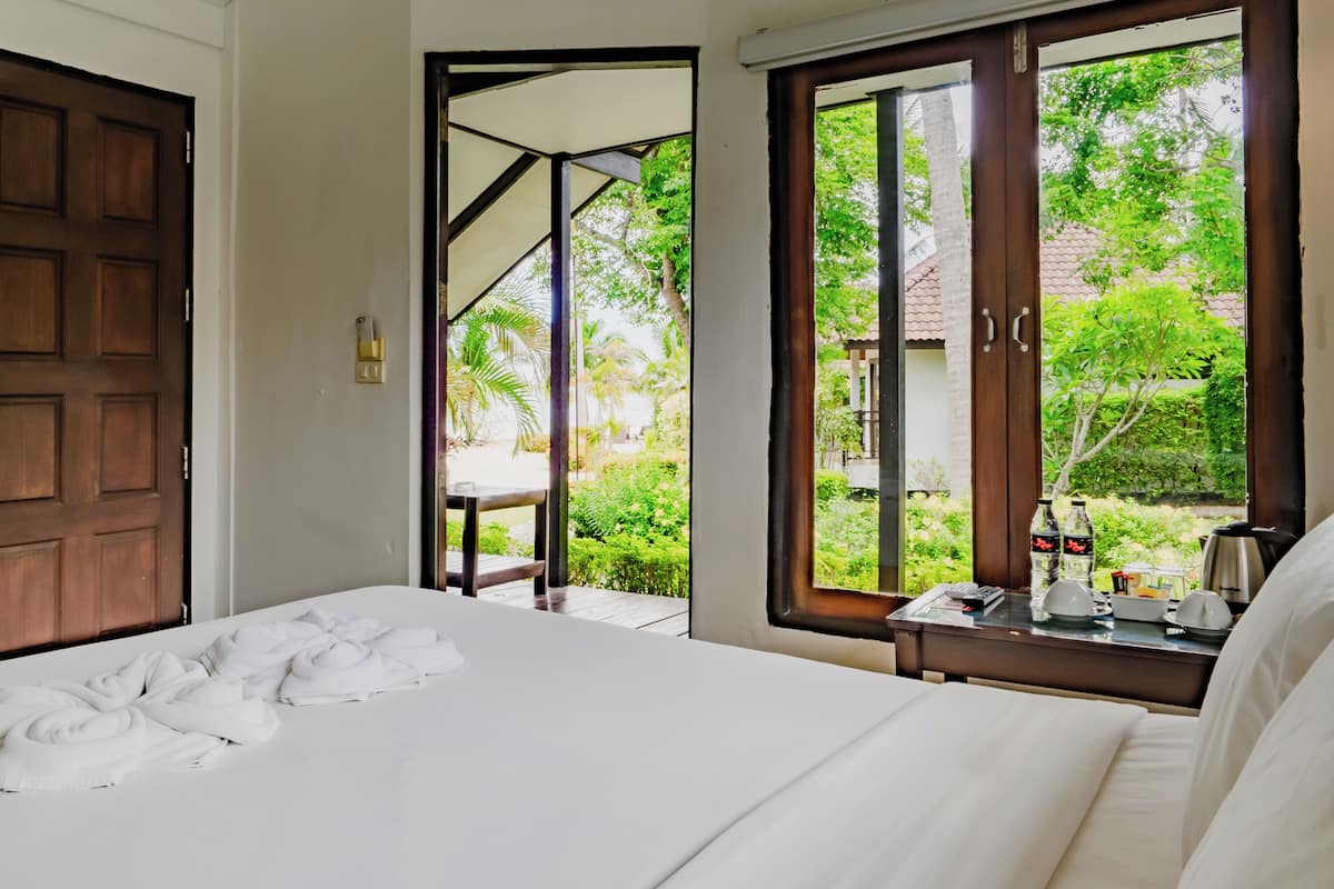 A hotel room with a bed, a nightstand with a coffee maker, and a view of a garden through the window.