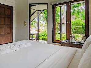 A hotel room with a bed, a nightstand with a coffee maker, and a view of a garden through the window.