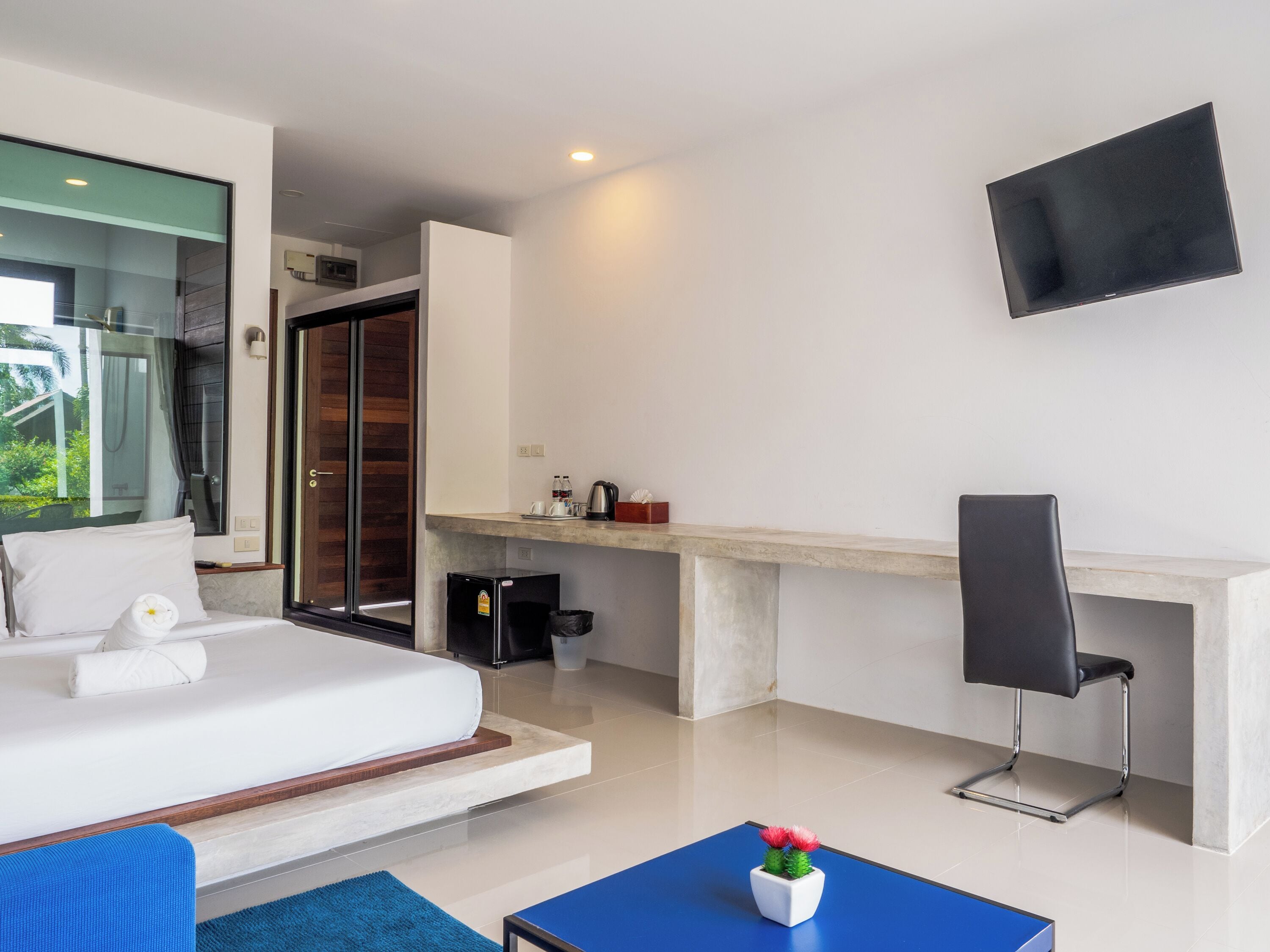 A modern hotel room with a bed, a desk, a chair, and a TV mounted on the wall.