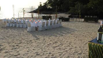 Montaje de comedor frente al mar, con manteles y sillas blancas, preparado para un evento.