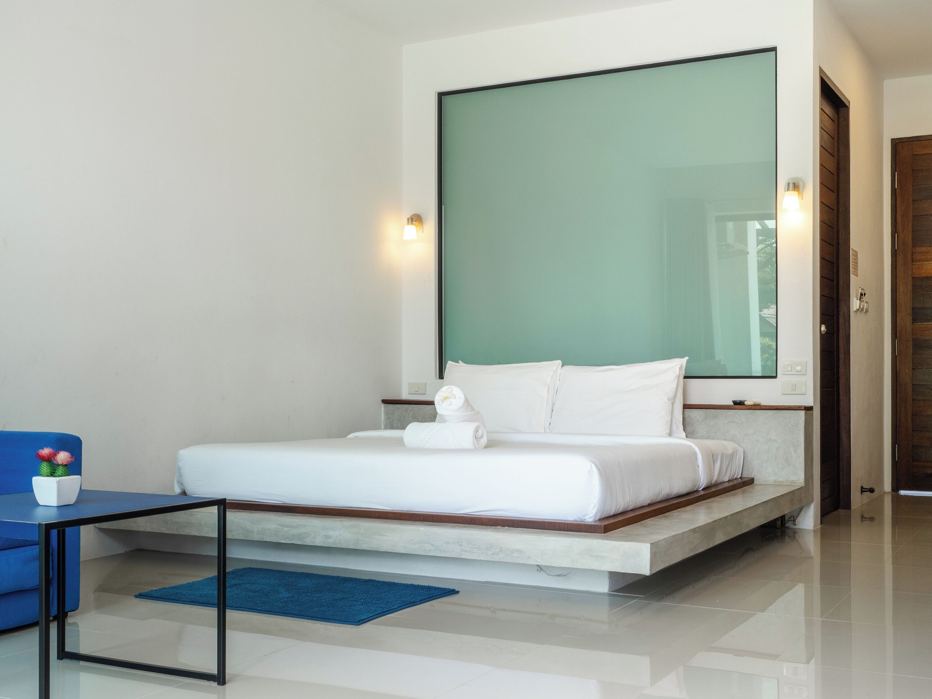 A modern bedroom with a large bed, a blue sofa, and a small potted plant.