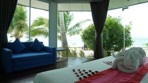 A bedroom with a large bed, a blue sofa, and a view of the beach and palm trees. - Am Samui Resort (Koh Samui)