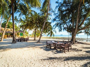 A beach with wooden tables and chairs, palm trees, and a thatched-roof hut.