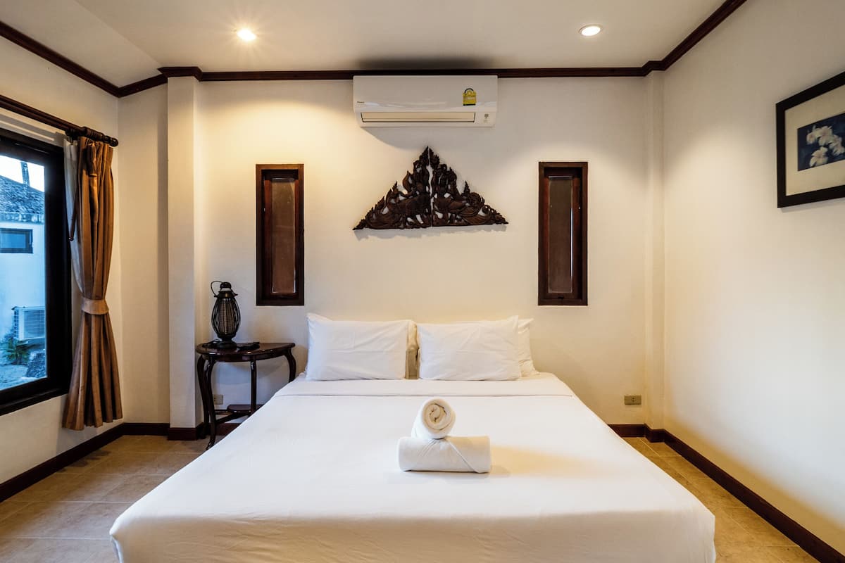A hotel room with a large bed, a window with curtains, an air conditioning unit, and a decorative wall piece.