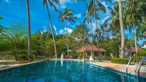 A clear blue swimming pool surrounded by palm trees and a small building with a tiled roof. - Am Samui Resort (Koh Samui)