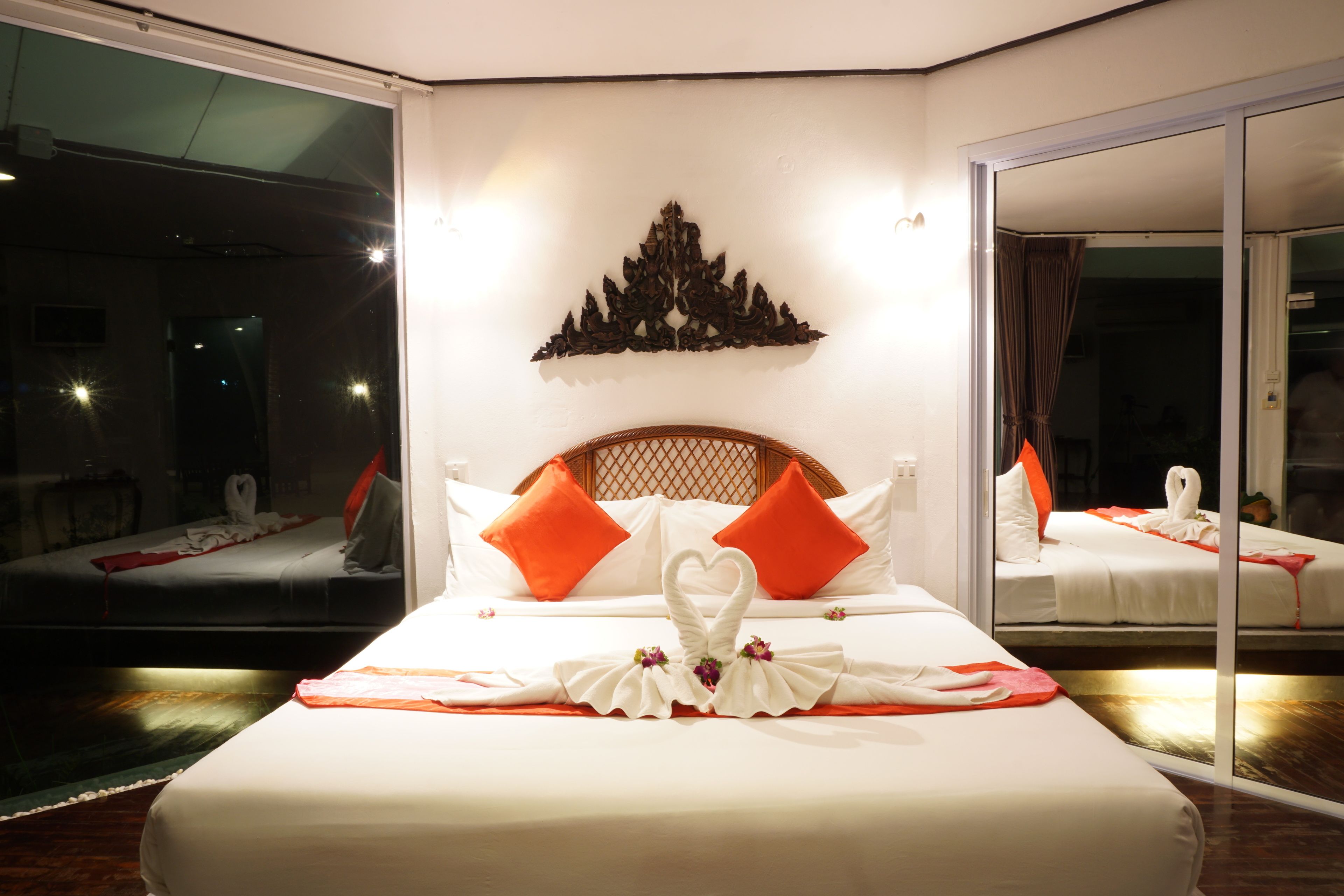A hotel room with a large bed, two orange pillows, a decorative wall piece, and a glass door leading to a balcony.