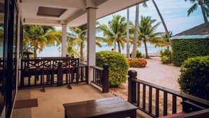 A covered outdoor area with a wooden table and chairs, palm trees, and a view of the beach. - Am Samui Resort (Koh Samui)