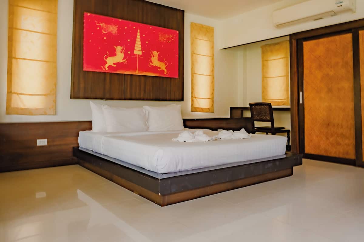 A modern hotel room with a large bed, a wooden headboard, and a red artwork above the bed.