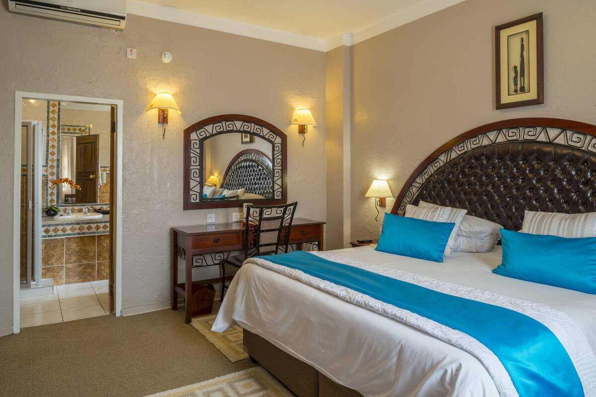 Ein Hotelzimmer mit einem großen Bett, einem Schreibtisch mit Stuhl, einem Spiegel und zwei Wandlampen.