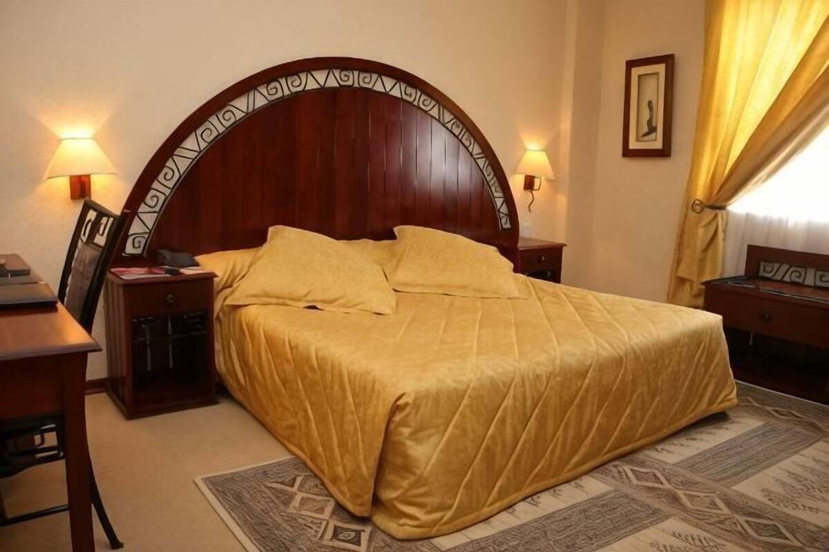 Ein Hotelzimmer mit einem großen Bett, zwei Nachttischen, einem Schreibtisch und einem Stuhl.