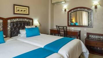 A hotel room with a large bed, a desk, a chair, a mirror, and a framed picture on the wall.