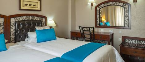 A hotel room with a large bed, a desk, a chair, a mirror, and a framed picture on the wall.