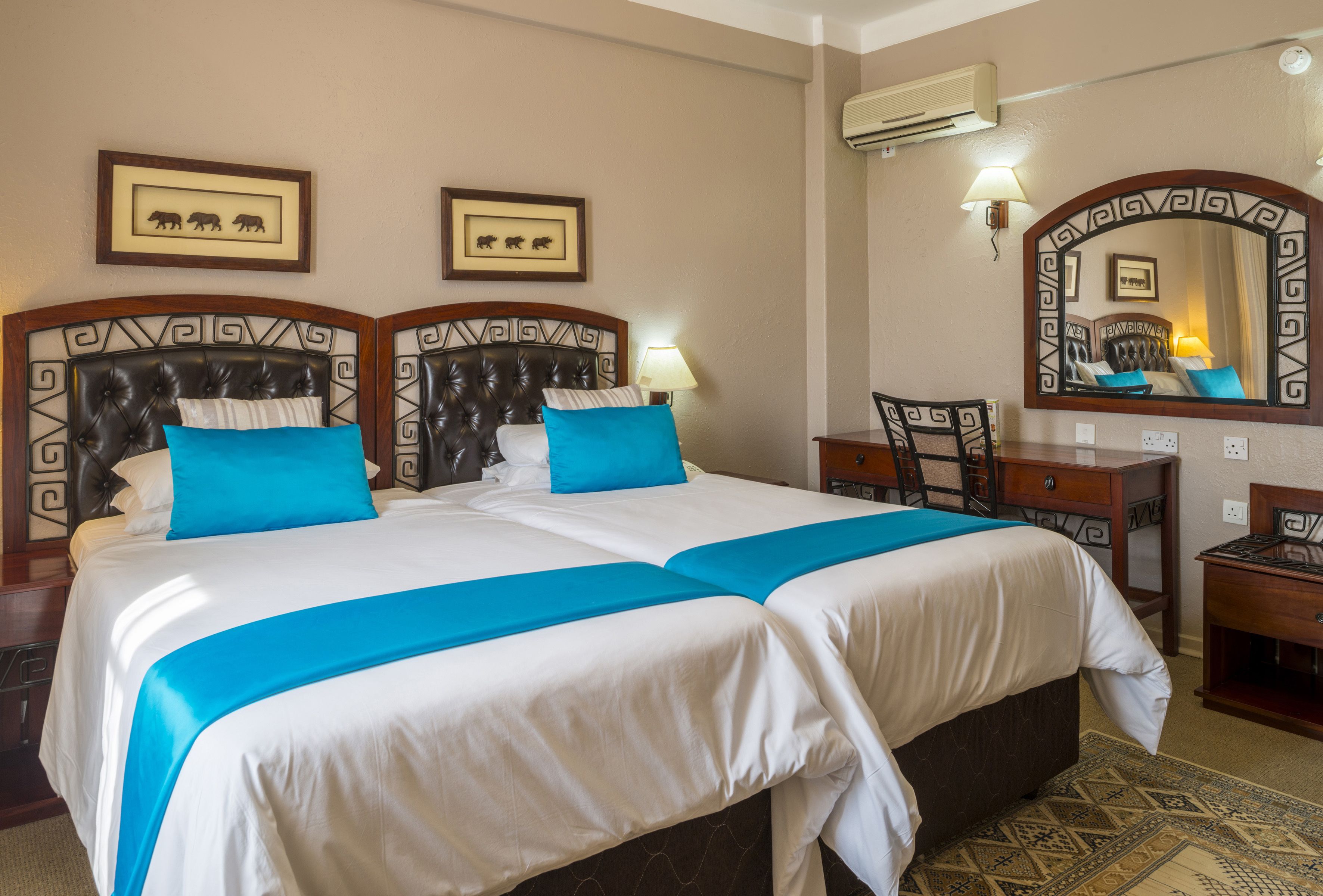 A hotel room with a large bed, two bedside tables, a desk, a chair, a mirror, and framed pictures on the wall.