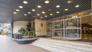 Entrada de um edifício moderno com fachada de mármore, portas de vidro e guarda-corpo de metal.