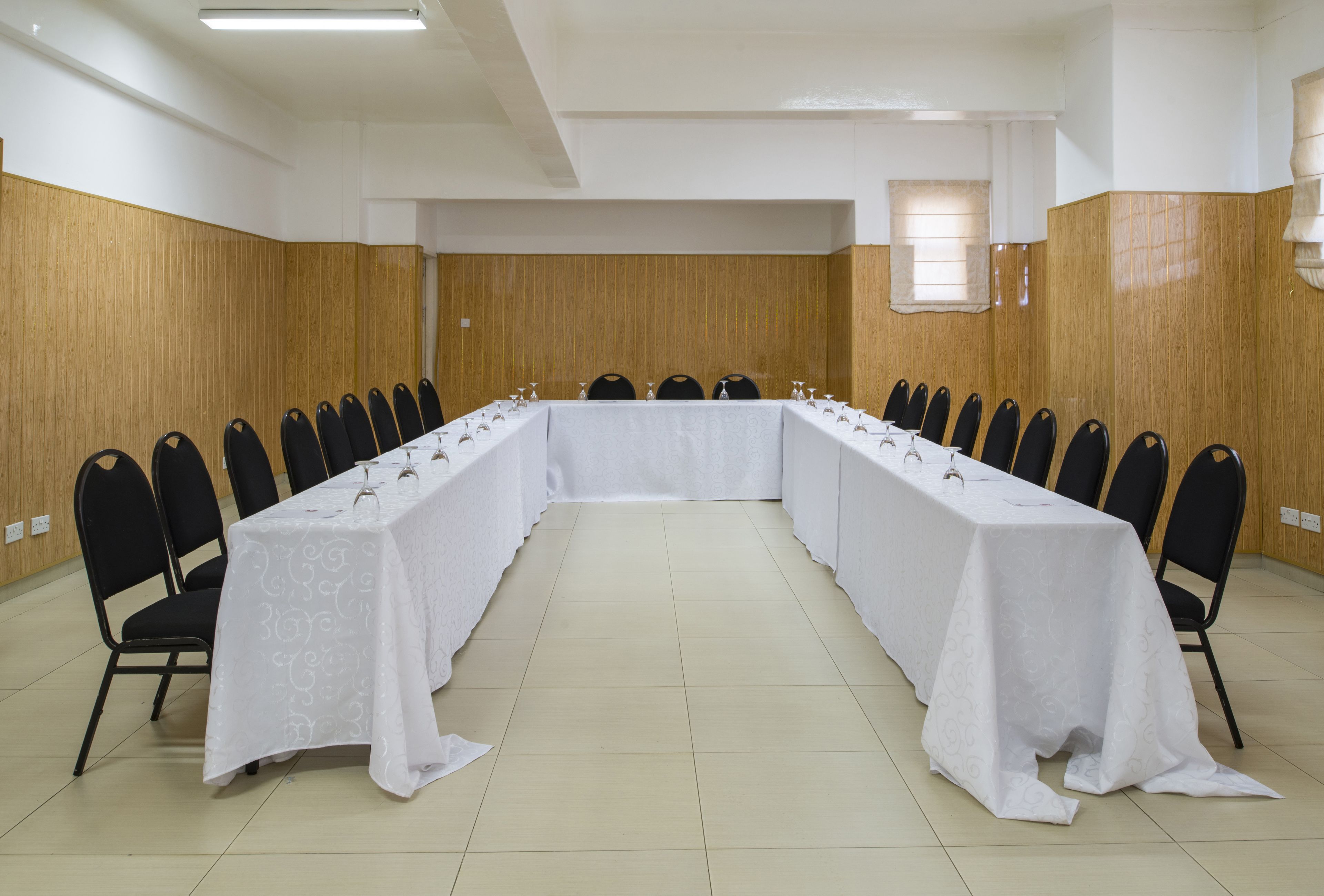 A conference room with a long table, black chairs, and white tablecloths.