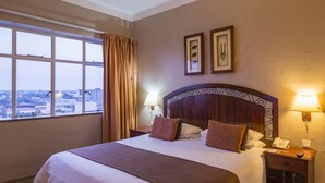 Quarto de hotel com uma cama grande, vista para a cidade e mesa de cabeceira com telefone.