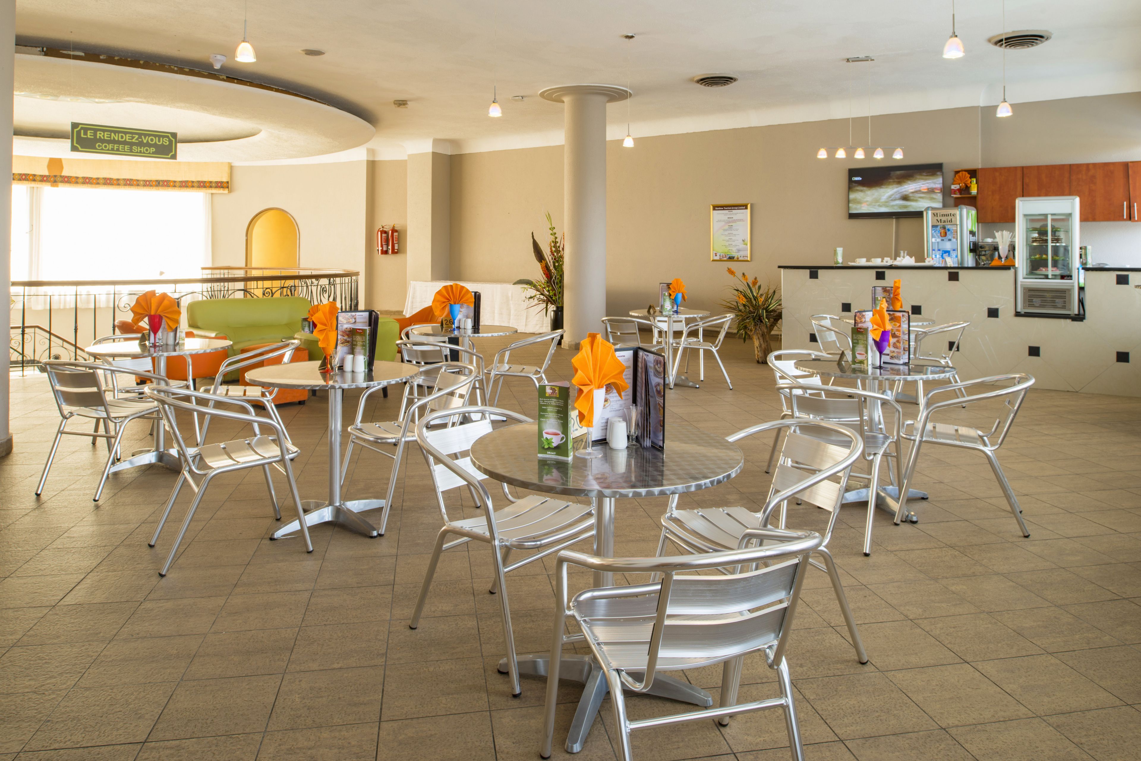 A spacious indoor area with multiple round tables and chairs, a coffee shop sign, and a kitchen area in the background.