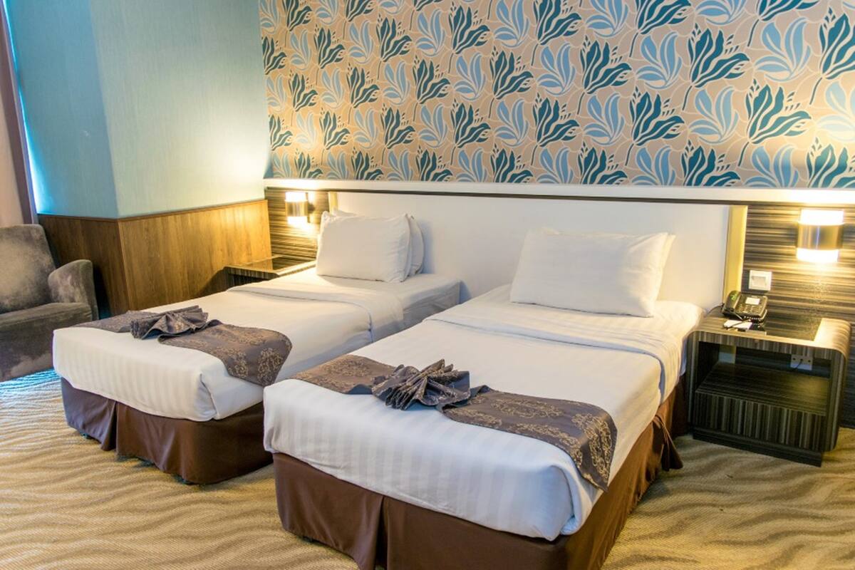 Una habitación de hotel con dos camas, un papel tapiz estampado, un sofá y una mesita de noche con un teléfono.