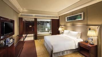 Une chambre d’hôtel avec un grand lit, une télévision, un bureau avec une lampe et une vue sur la ville, visible à travers une porte vitrée.