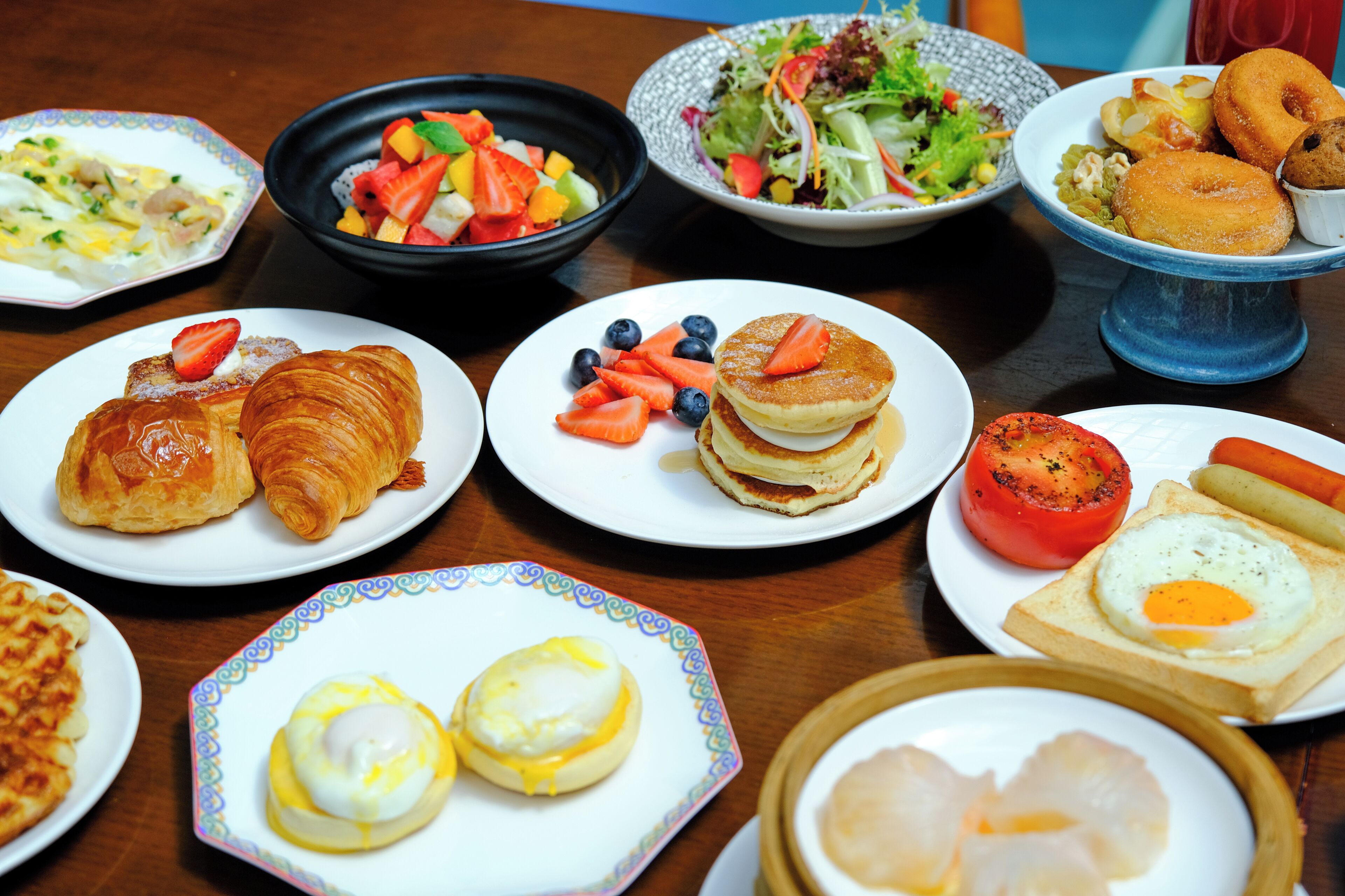 A table with various breakfast dishes including croissants, pancakes, eggs, and fruit.