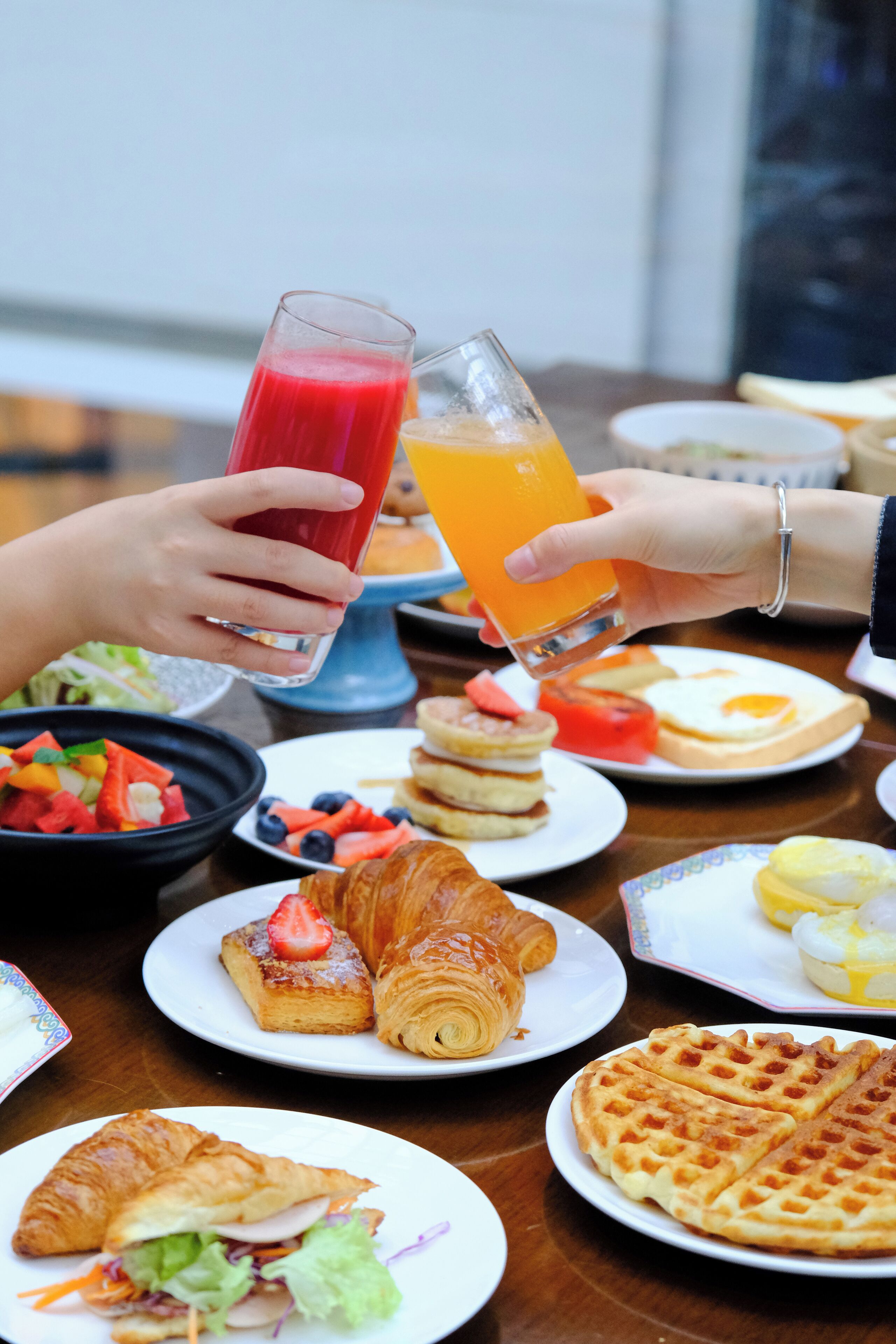 A breakfast setting with various dishes including waffles, croissants, and a fruit salad.