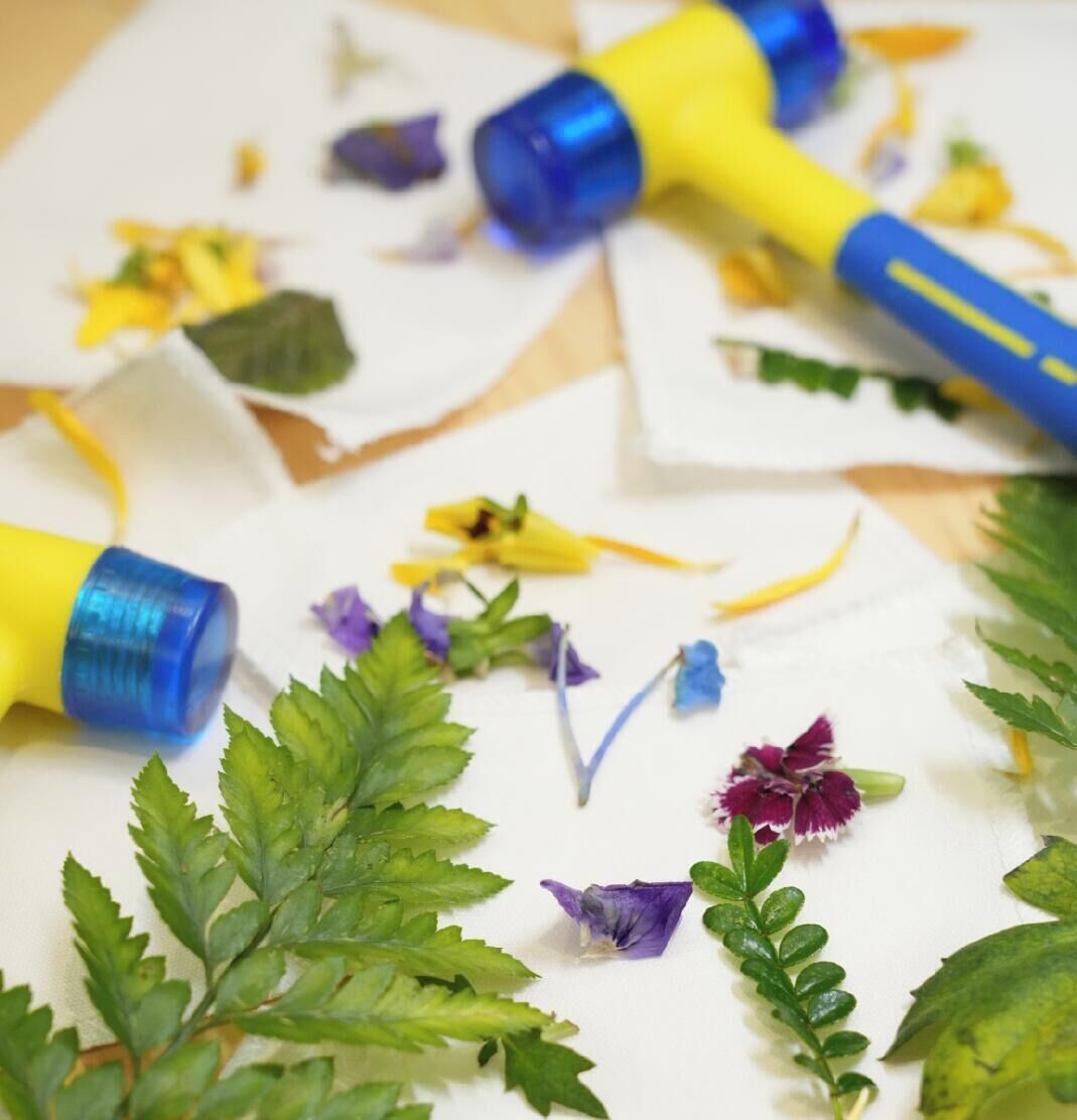 En overflade med hvide elementer, blå og gule objekter, grønne blade og lilla blomster.