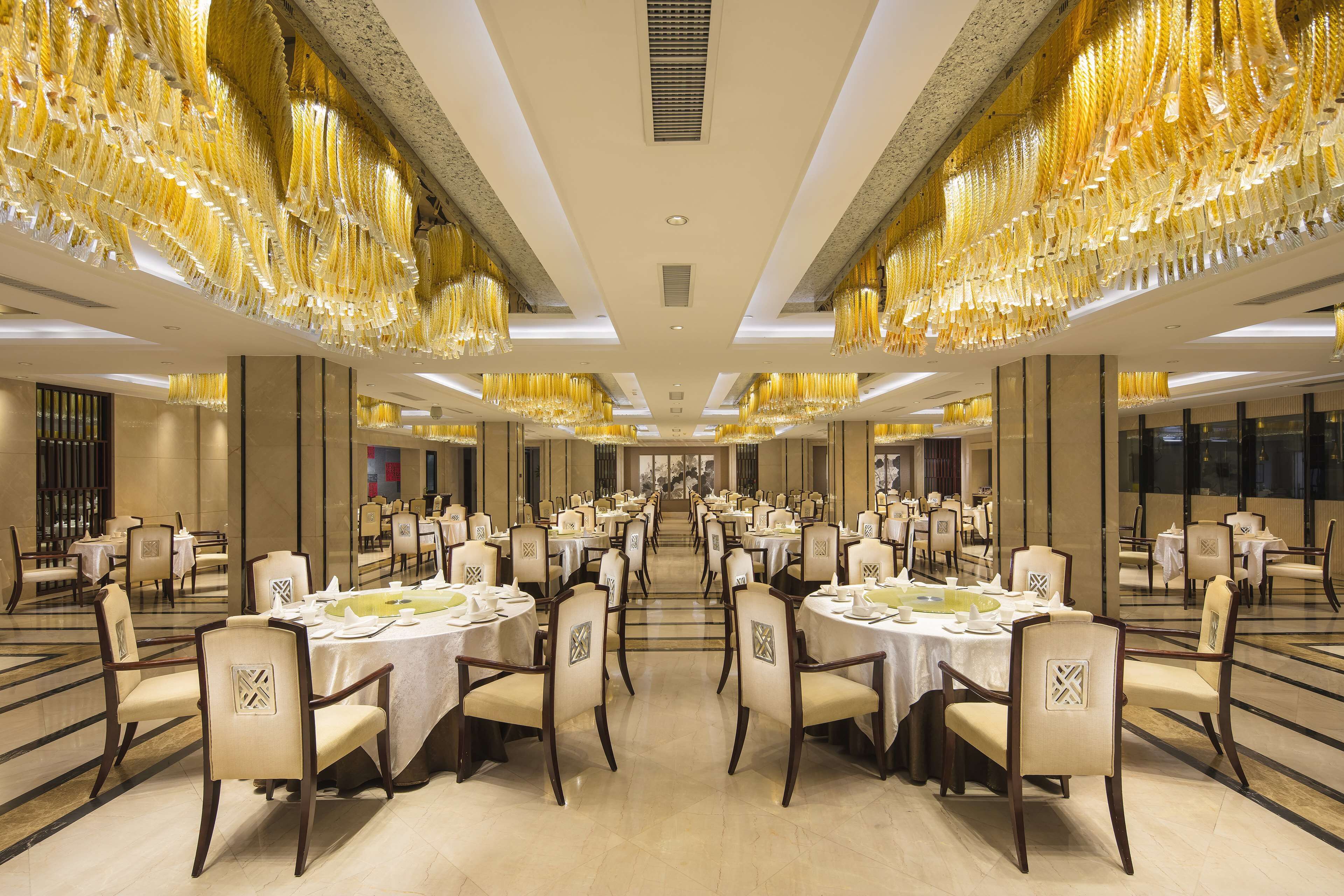 A spacious banquet hall with round tables and chairs, high ceilings, and ornate chandeliers.