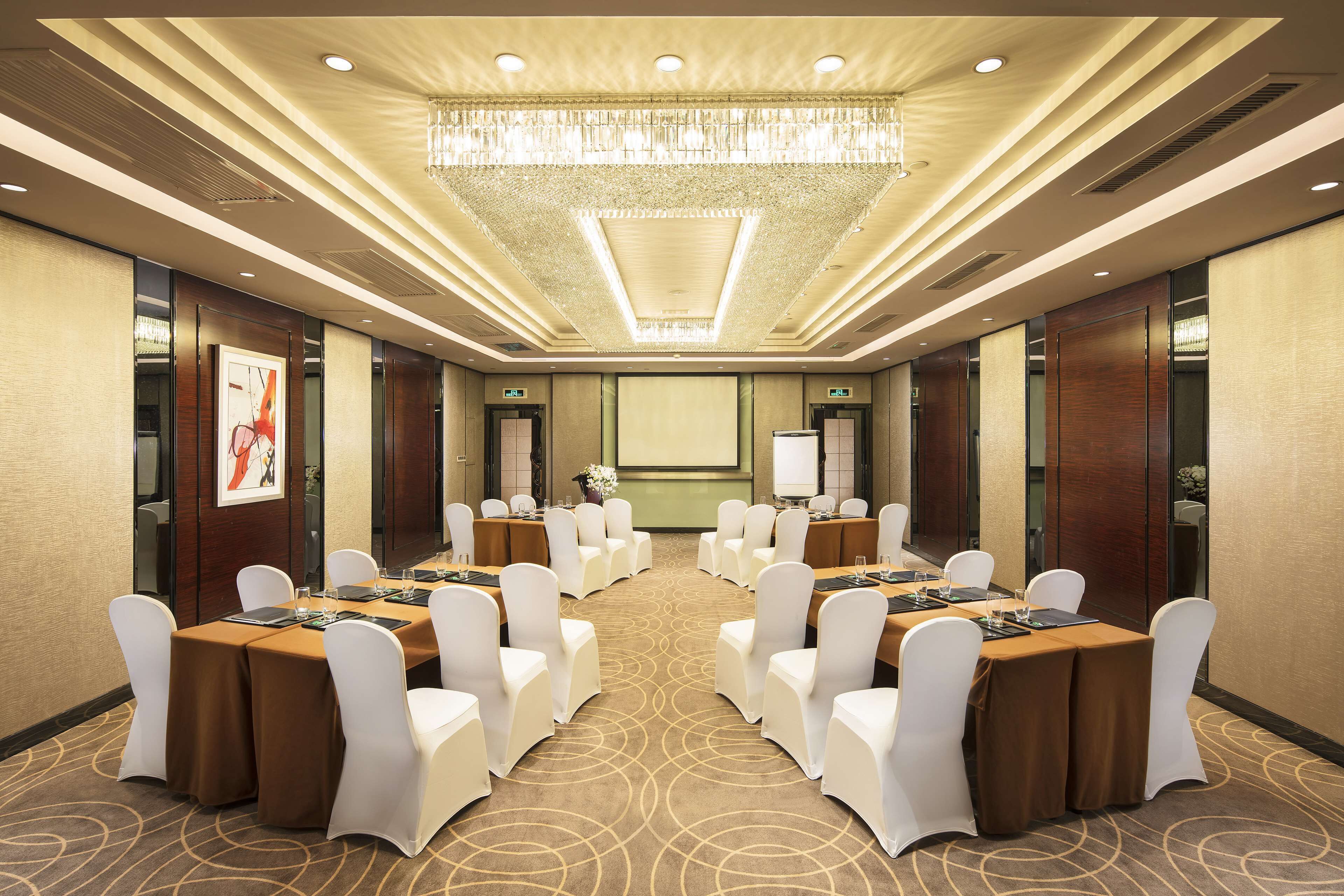 A conference room with round tables, white chairs, and a large chandelier.