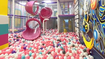 A colorful indoor play area with a ball pit, slides, and a wall with abstract designs.