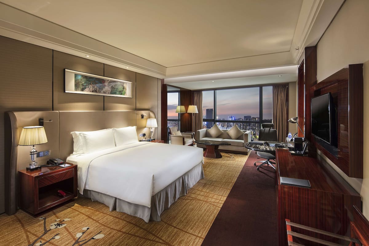 Habitación de hotel con una cama grande, un escritorio, televisión y vistas a la ciudad.