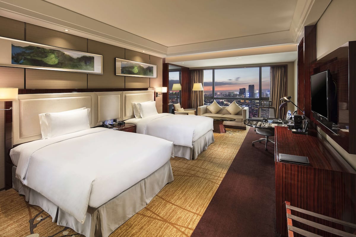 Habitación de hotel con dos camas, un escritorio, un televisor y vistas a la ciudad.