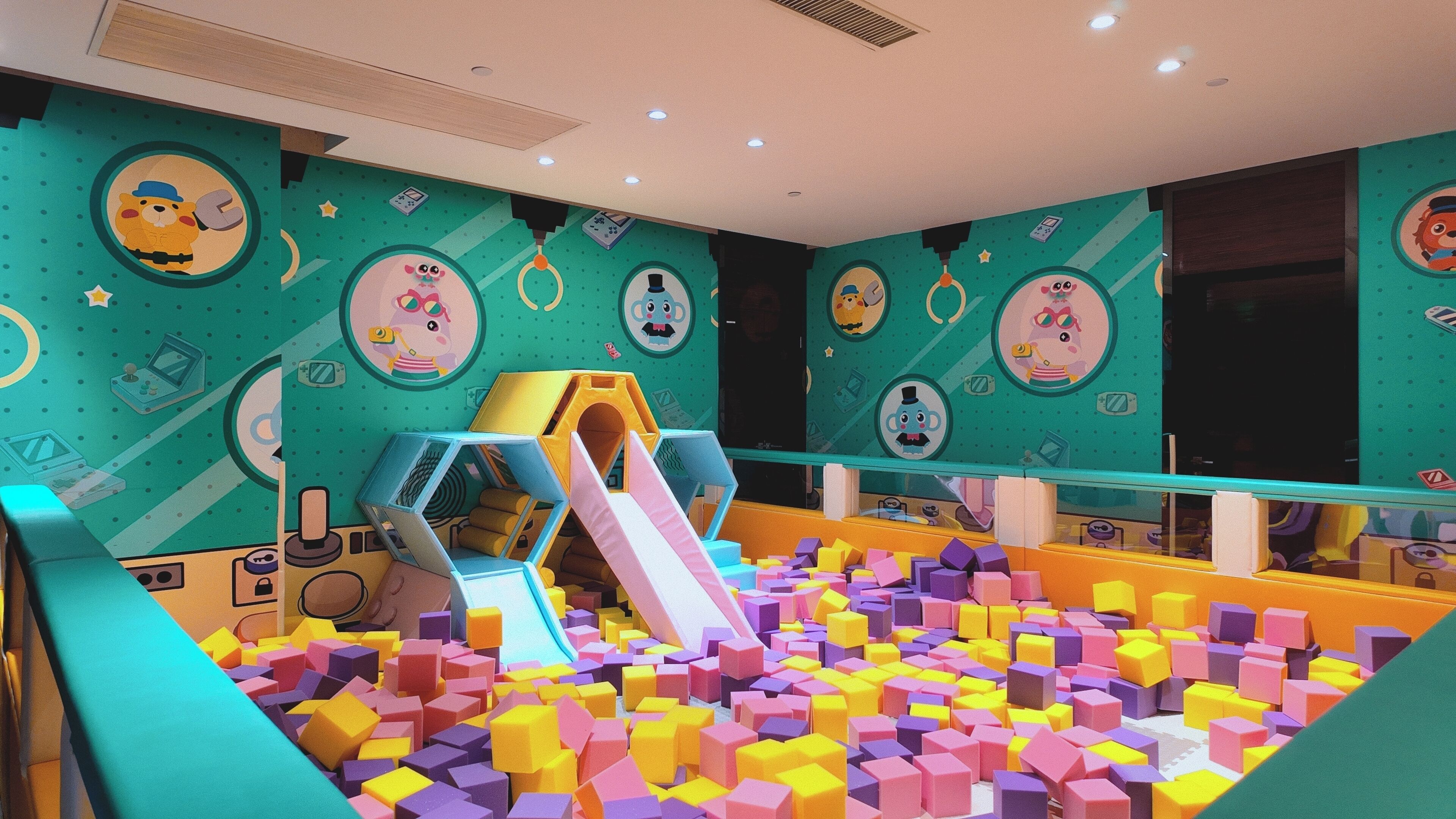 A children's play area with colorful foam blocks, a slide, and cartoon-themed wall decorations.
