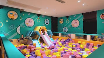 Un área de juegos infantiles con bloques de espuma de colores, un tobogán y decoraciones de pared con motivos de dibujos animados.