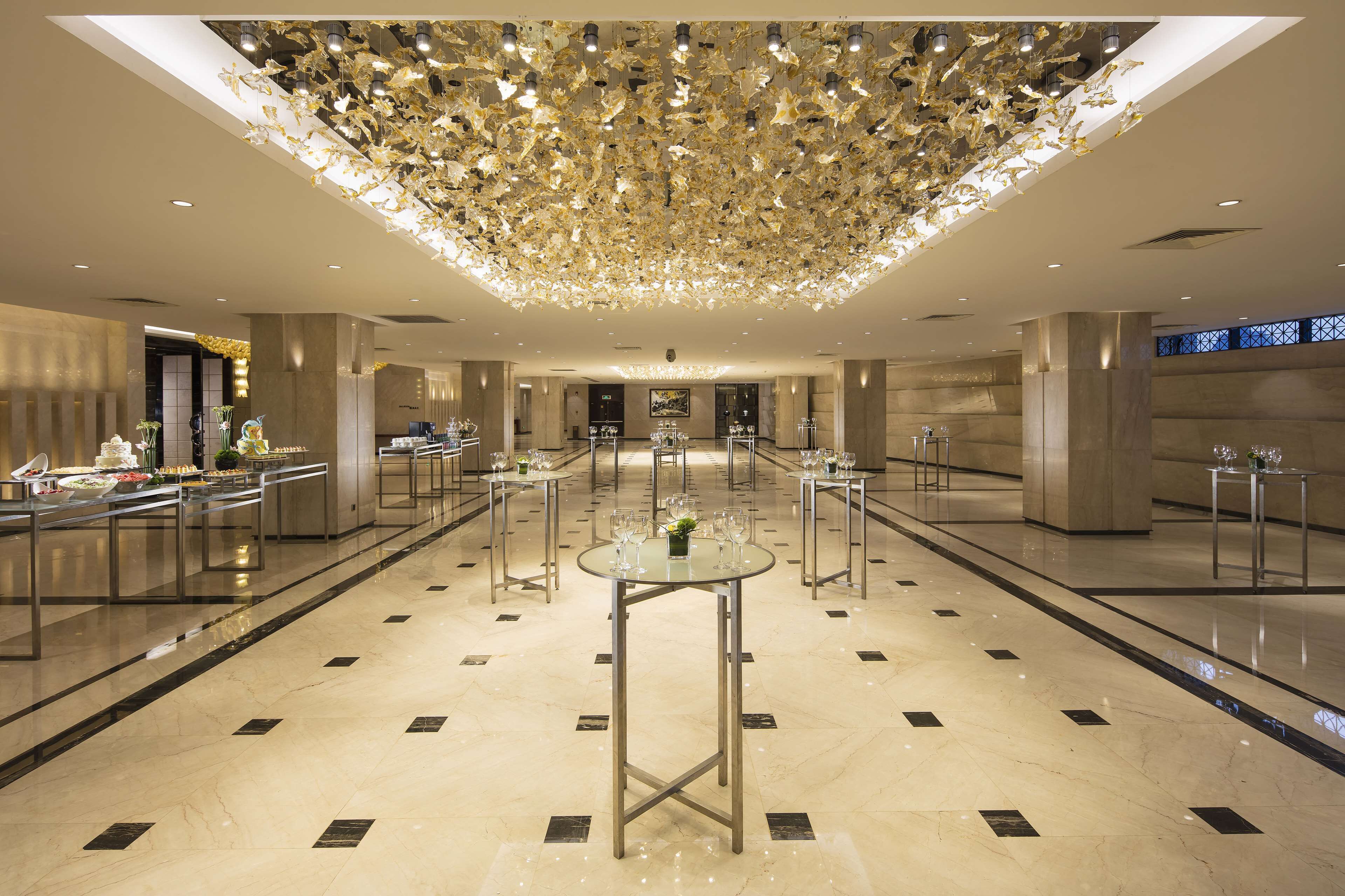 A spacious lobby with a high ceiling, reflective marble floors, and multiple tables with glass tops.