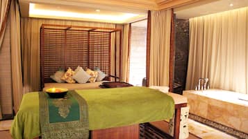 Une chambre d’hôtel avec un lit, une couvre-lit verte, une tête de lit en bois, une grande fenêtre et une baignoire en marbre.