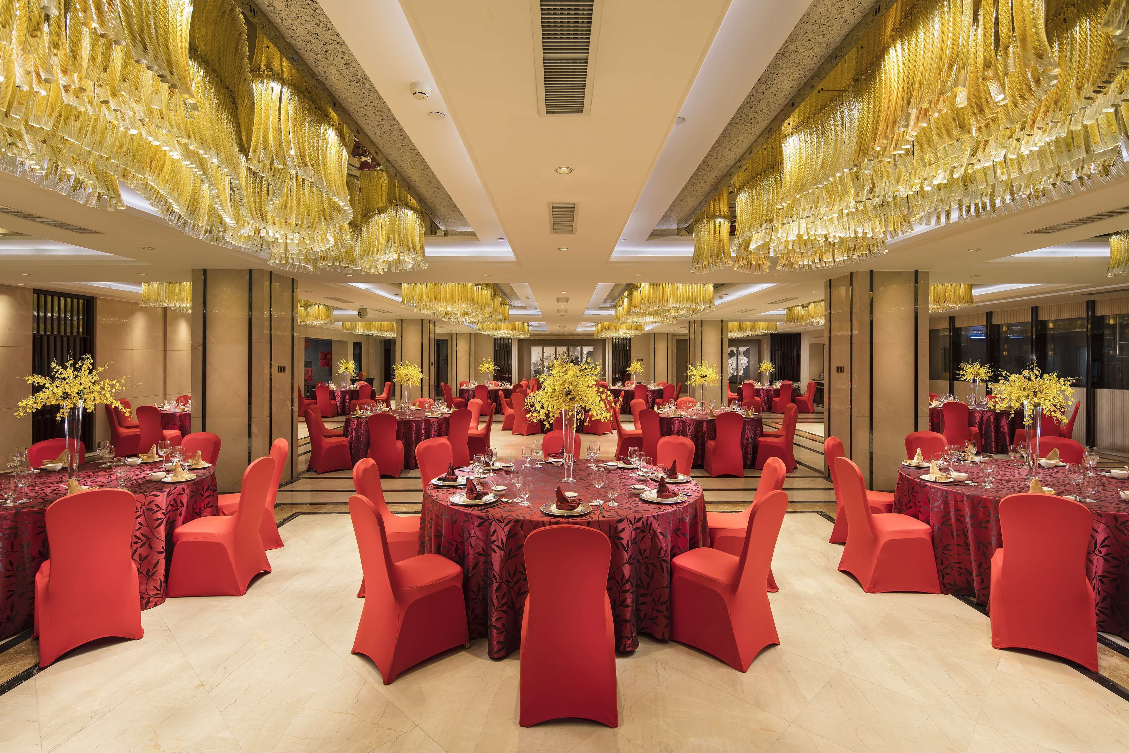 A banquet hall with round tables, red chairs, and golden chandeliers.
