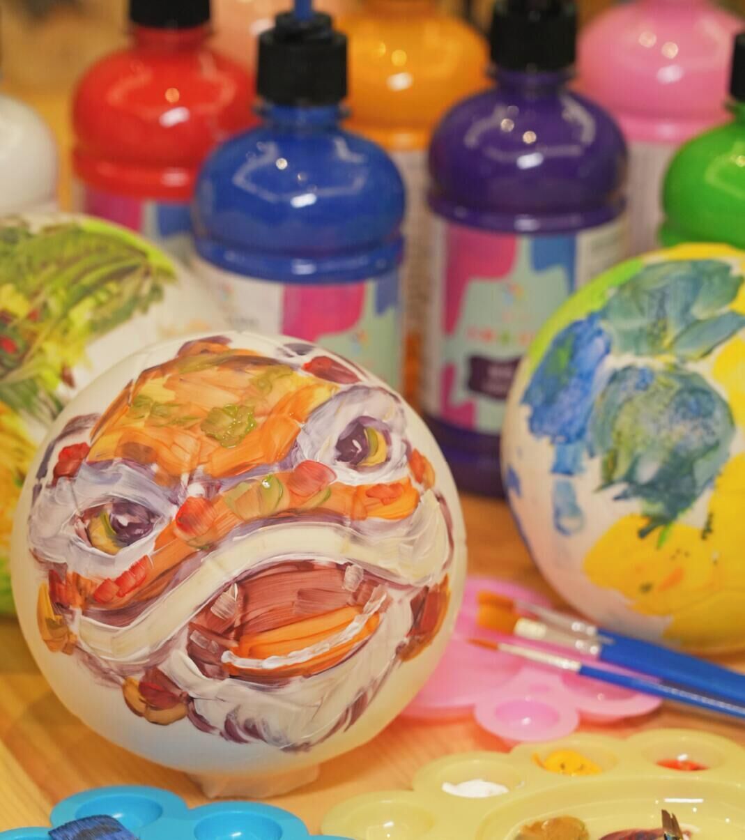 A close-up of a painted object with a face, surrounded by various paint bottles.