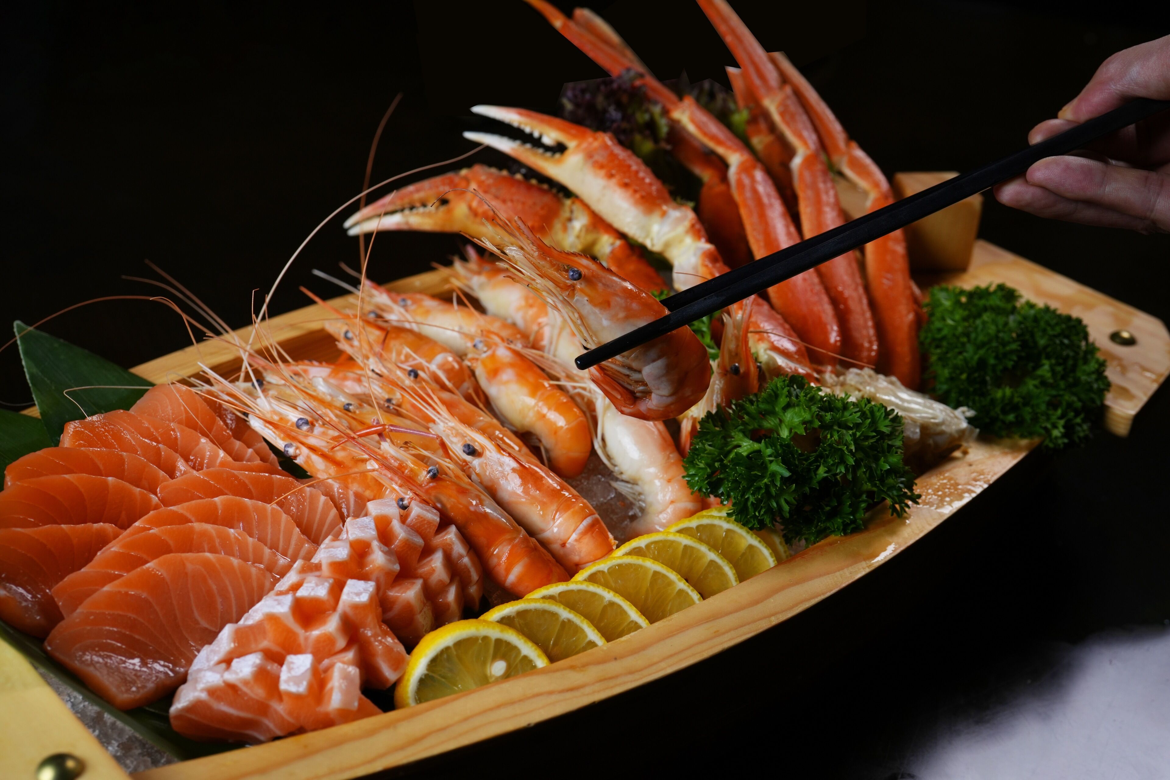A wooden tray with various seafood including prawns and salmon, garnished with lemon slices and parsley.